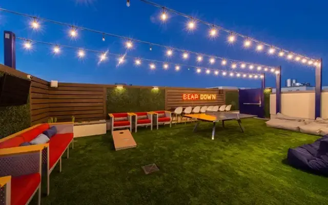 Stylish Rooftop Lounge A cozy rooftop lounge area featuring string lights, green turf, red seating, and a cornhole game setup.