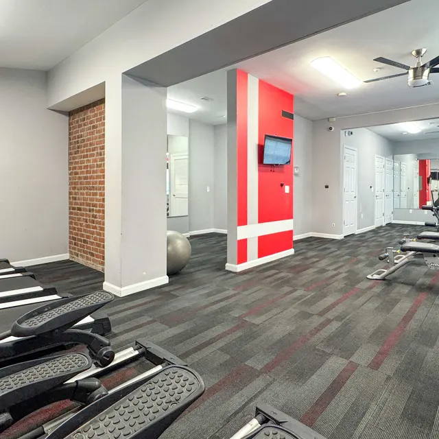 Interior view of a modern gym featuring fitness equipment, a brick wall, and a bright color scheme with red accents.