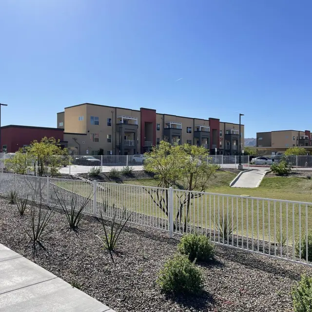 A view of a modern apartment complex with surrounding landscaped area, featuring grassy fields and decorative plants.