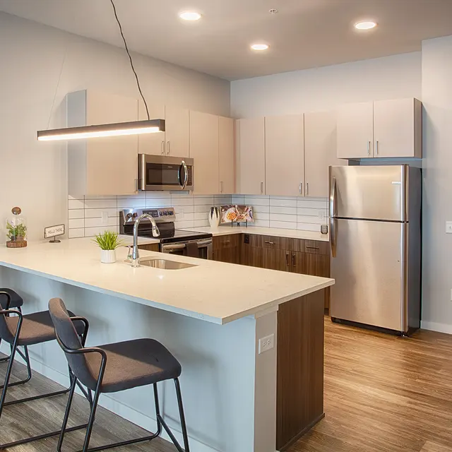 Modern kitchen with gray cabinets, stainless steel appliances, a large island with seating, and hardwood flooring.