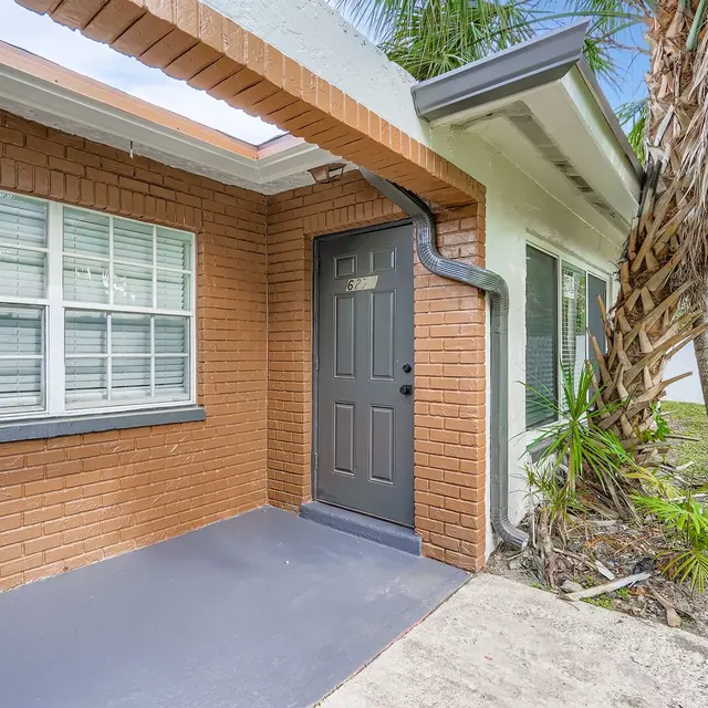 Front entrance of a building featuring a gray door and multiple windows, surrounded by palm trees.
