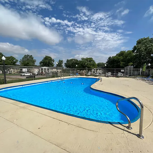 Swimming Pool with Lounge Chairs A well-maintained swimming pool with clear blue water, surrounded by a fenced area. Several lounge chairs are positioned nearby, and the sky is partly cloudy.