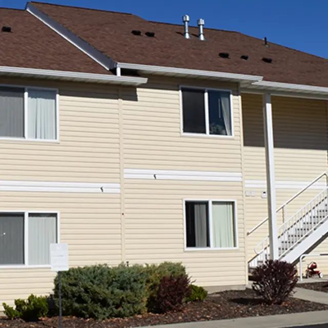Two-Story Residential Building Exterior Exterior view of a two-story residential building with light-colored siding, white trim, and a staircase leading to the upper level.