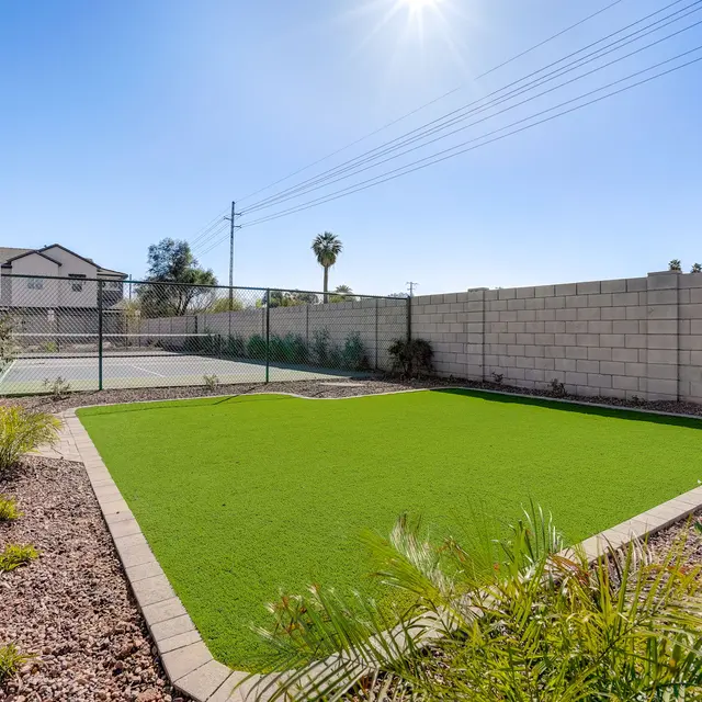Outdoor Lawn and Tennis Court Area A bright outdoor area featuring a well-maintained green lawn and a tennis court in the background. The sky is clear with the sun shining brightly.