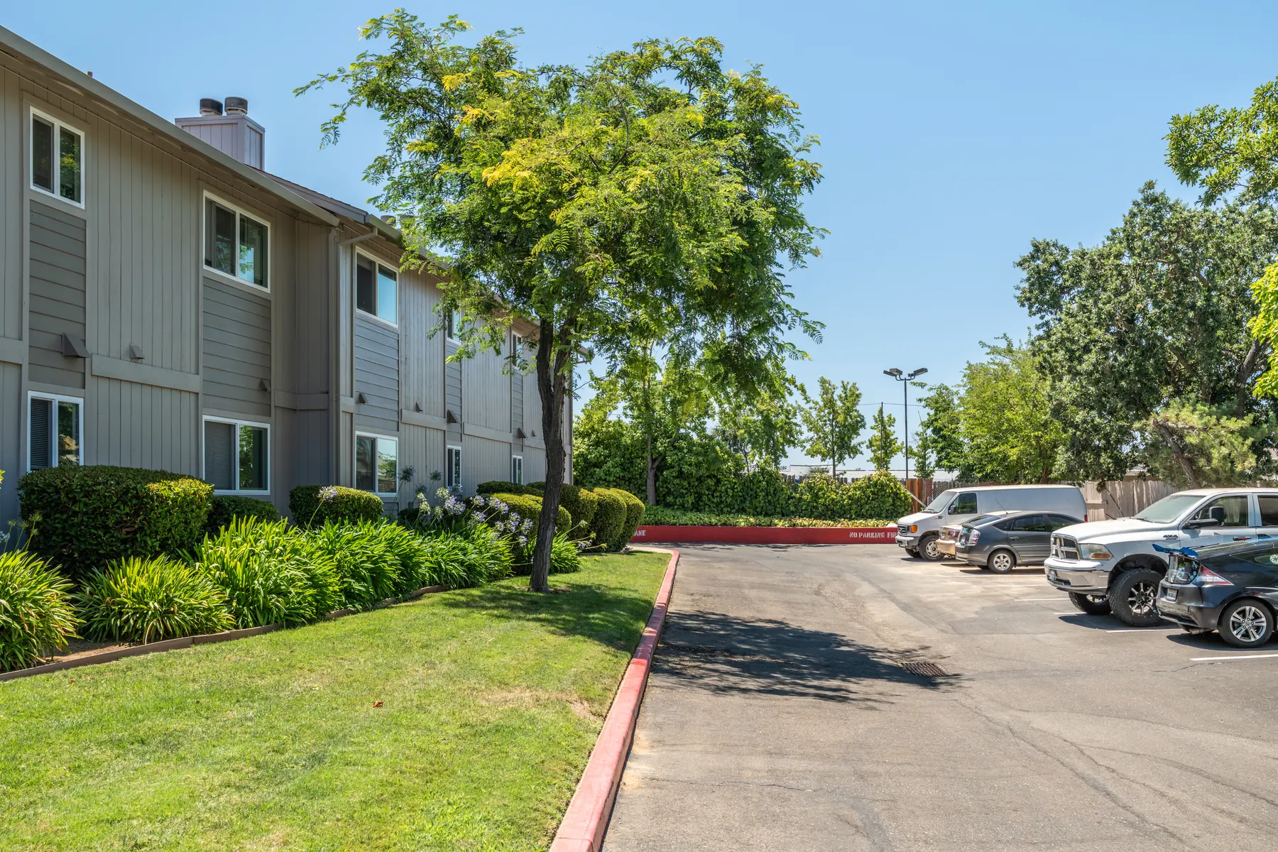 Exterior view of a hotel with parking area and green landscaping on a sunny day.