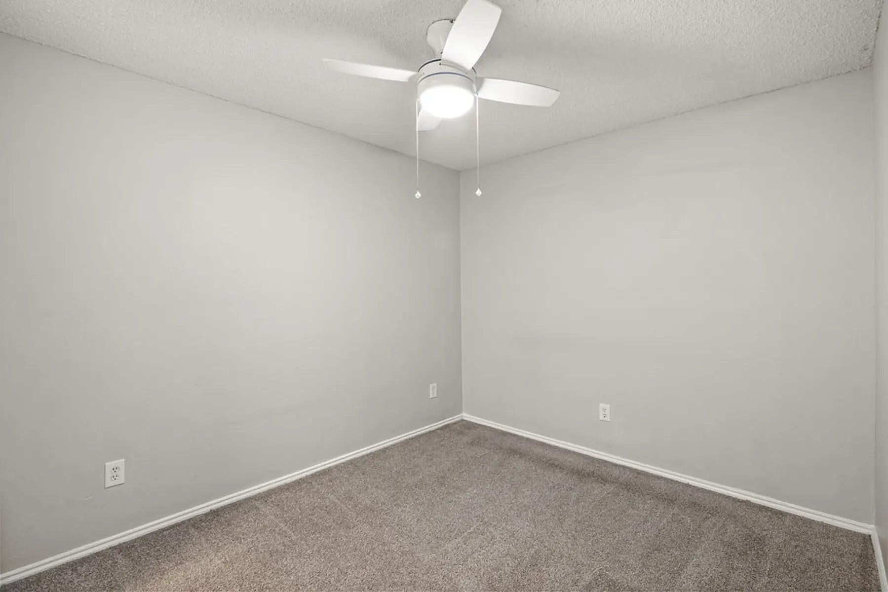 Empty Room With Ceiling Fan A vacant room with light gray walls, carpeted flooring, and a ceiling fan.