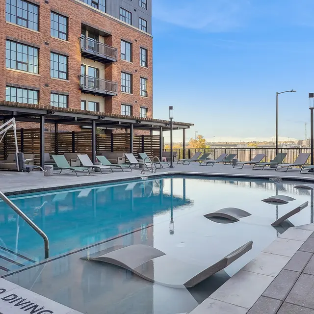 Modern Apartment Pool Area A modern swimming pool area with lounge chairs and a view of the city skyline in the background.