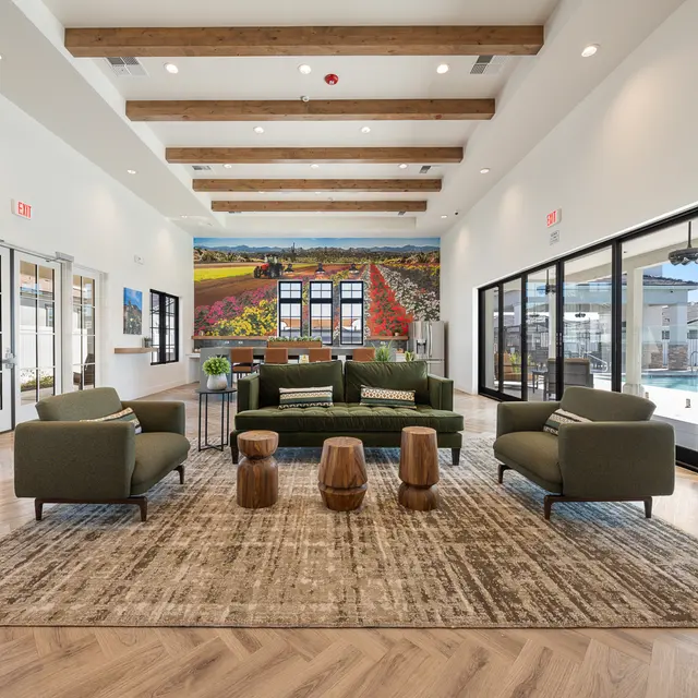 Modern lounge area with a green sofa, wooden stools, and a large mural, featuring an outdoor pool view through glass doors.