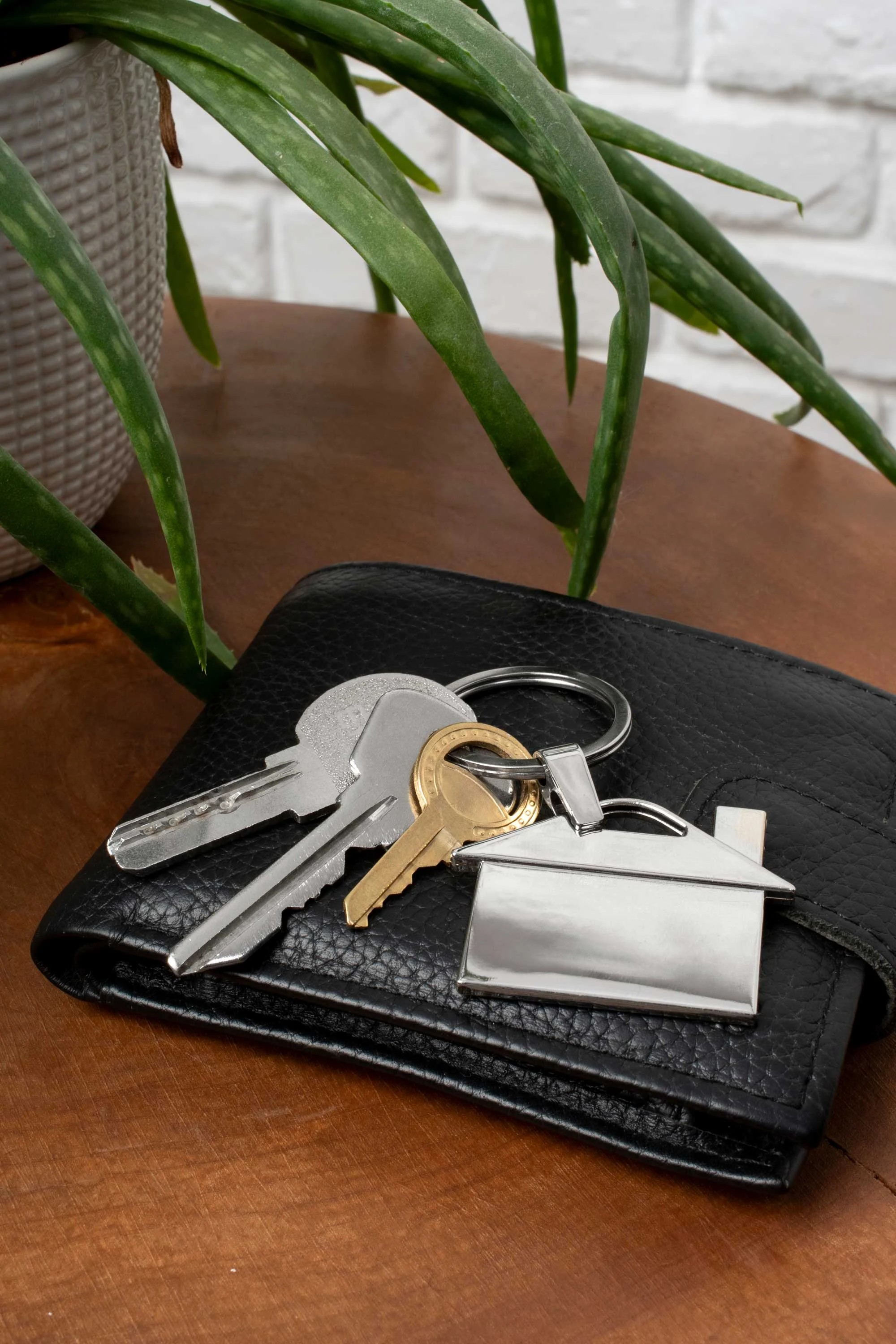 Keys and Wallet Arrangement A close-up of keys resting on a black wallet on a wooden surface, with a green plant in the background.