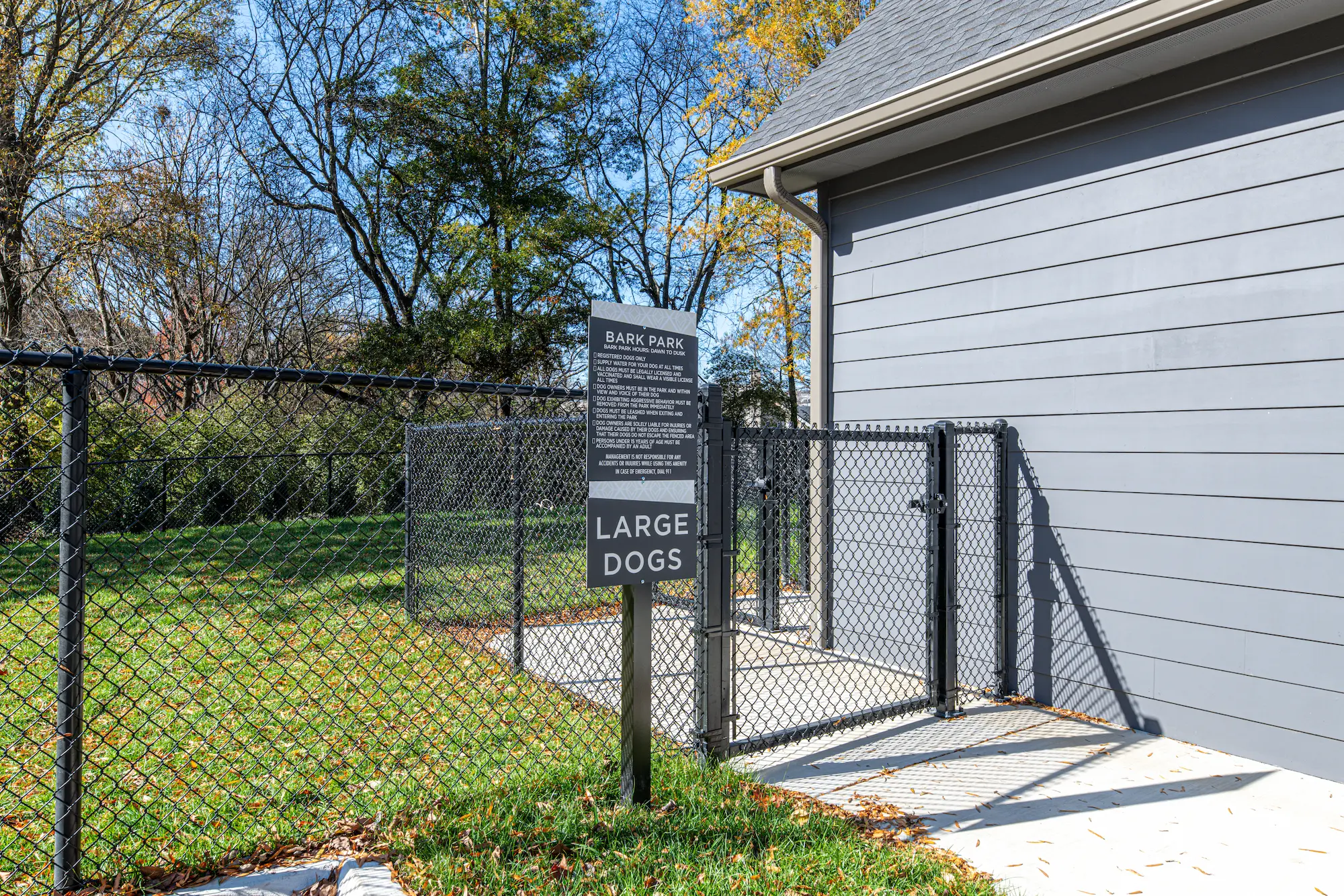 Bark Park for Large Dogs A fenced area labeled 'Bark Park' for large dogs, featuring a sign with rules and information, surrounded by greenery and trees.