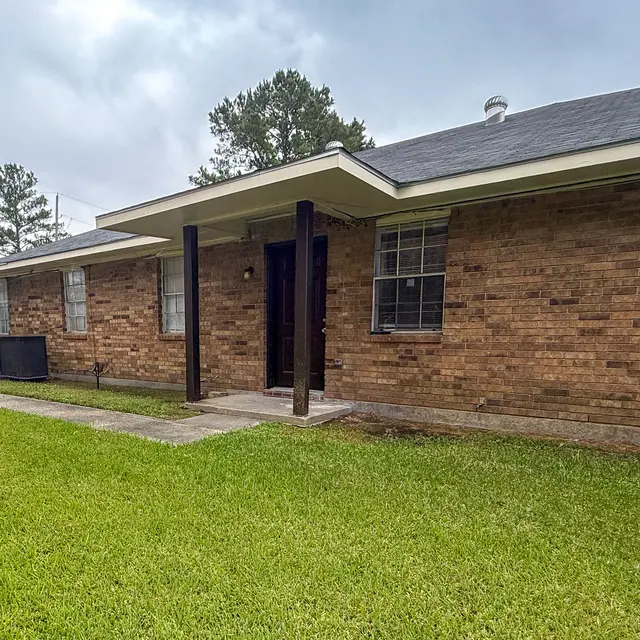 Front view of a red brick house with a grassy lawn and overcast sky.
