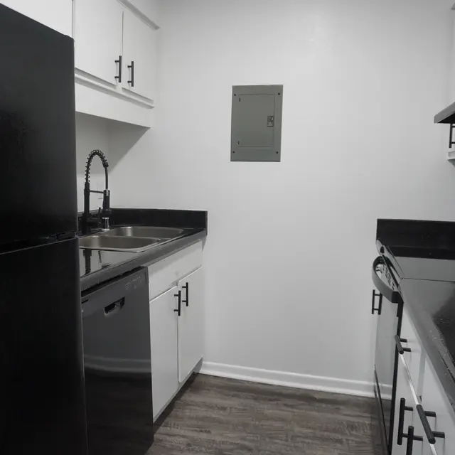 A modern kitchen featuring a black refrigerator, black stove, black countertop, and white cabinets against a light-colored wall.