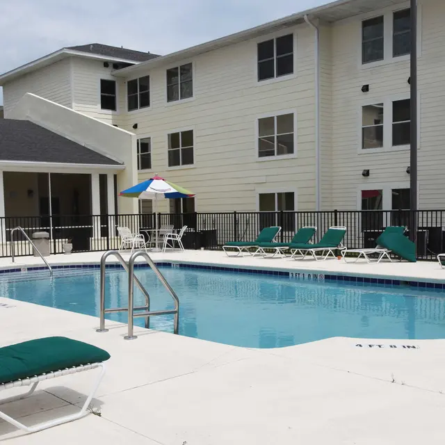 Outdoor swimming pool at an apartment complex with lounge chairs and umbrellas nearby.