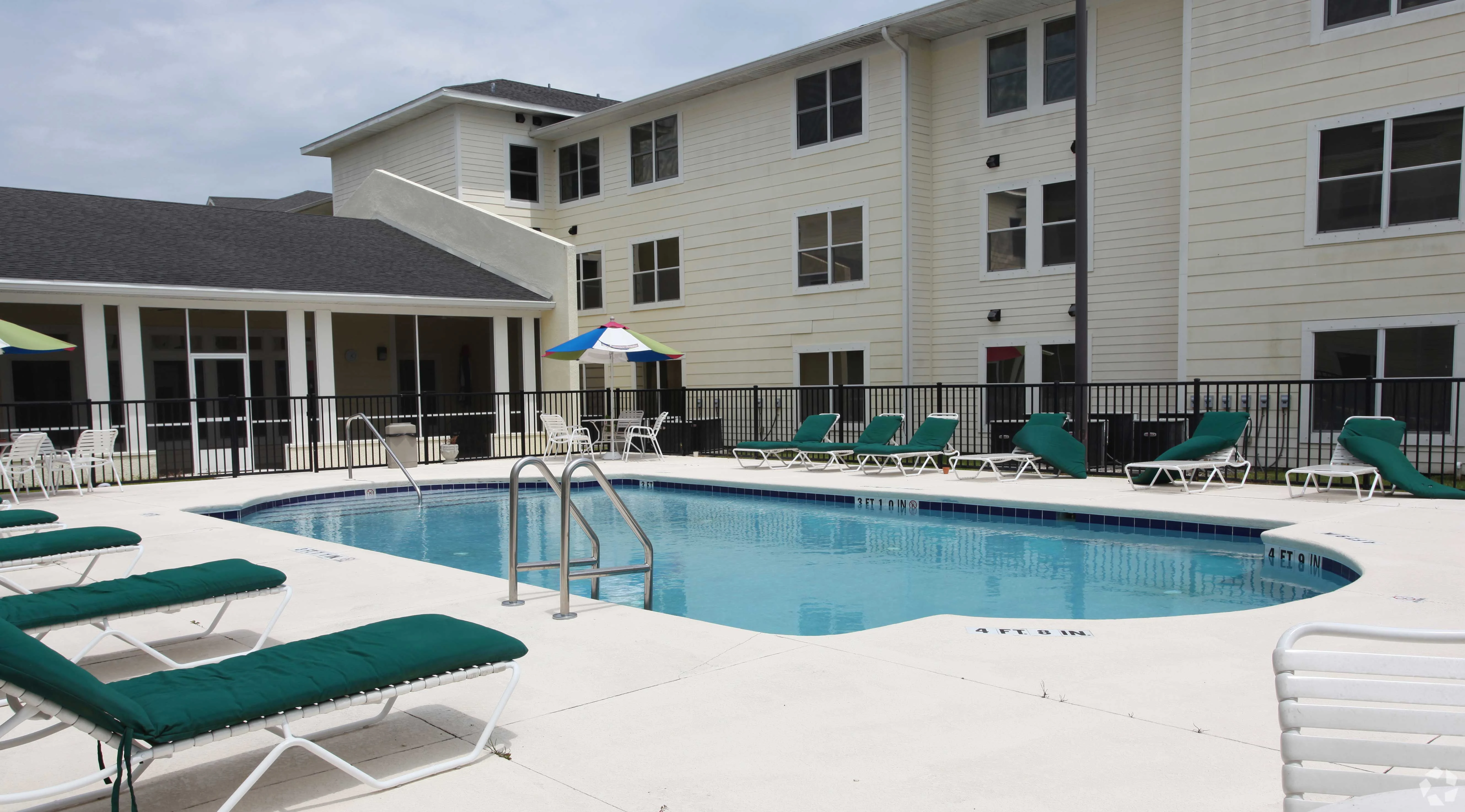 Outdoor swimming pool at an apartment complex with lounge chairs and umbrellas nearby.