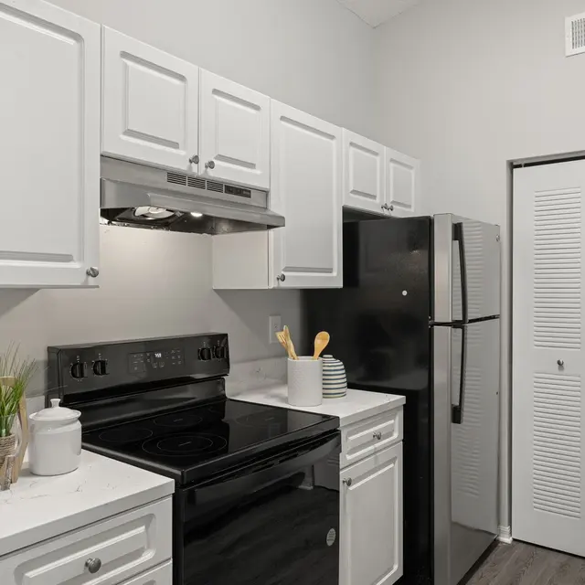 A modern kitchen featuring white cabinets, a black stove, and a black refrigerator. The countertops are white with gray veining, and there are kitchen utensils set on the counter.