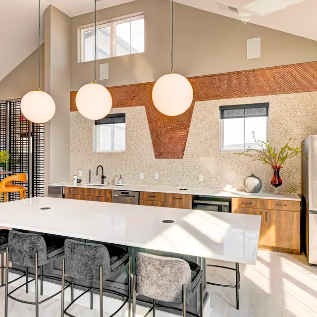 A modern kitchen with a large white island, bar stools, and pendant lighting. The walls are adorned with a textured copper accent.