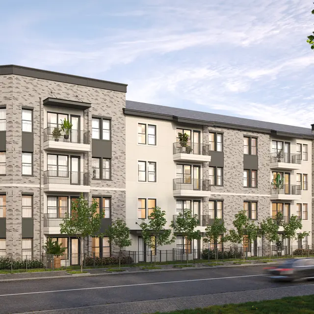 A modern four-story apartment complex with a stylish façade, featuring balconies and greenery in the foreground and a clear blue sky in the background.