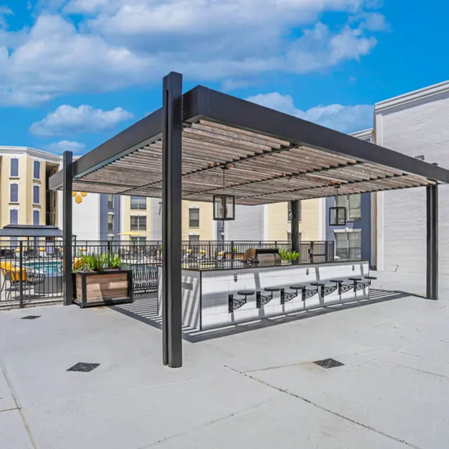 Outdoor covered seating area at an apartment complex with a swimming pool in the background.