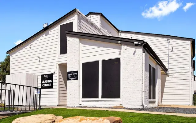 A modern leasing center for an apartment complex, featuring a light-colored exterior with large windows and a well-maintained lawn.