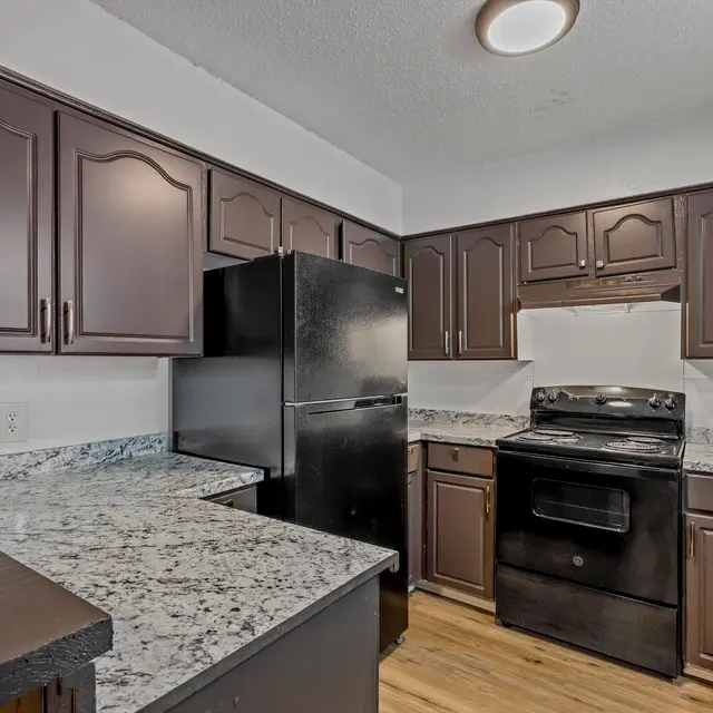 A modern kitchen featuring dark wood cabinets and black appliances, with granite countertops and wooden flooring.
