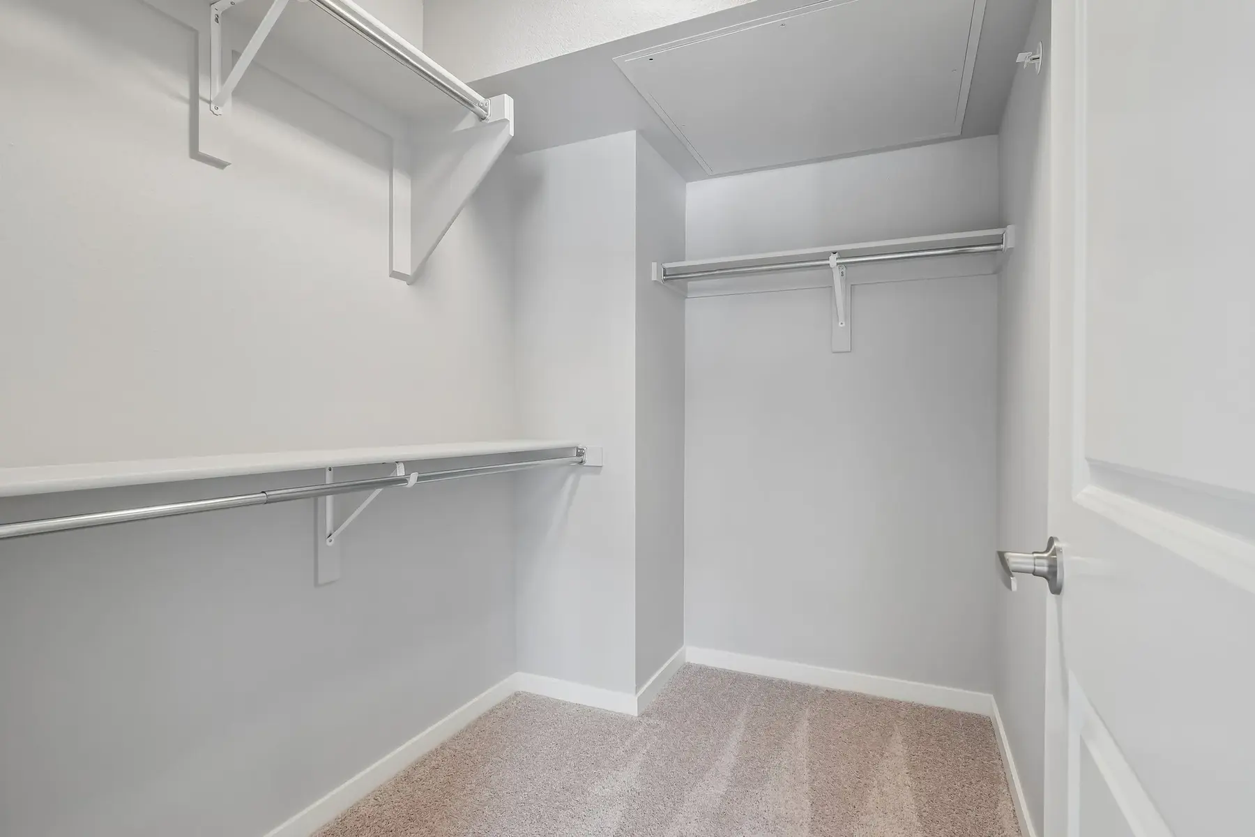 An empty closet with white walls and light-colored flooring, featuring wall-mounted hangers and a door.
