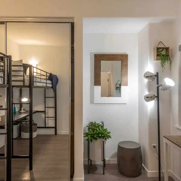 A modern bedroom featuring a bunk bed, a desk setup, a potted plant, and stylish lighting fixtures.