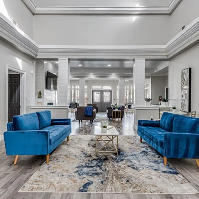 A modern lobby featuring blue sofas, a decorative rug, and stylish decor in a well-lit space with high ceilings and wooden flooring.
