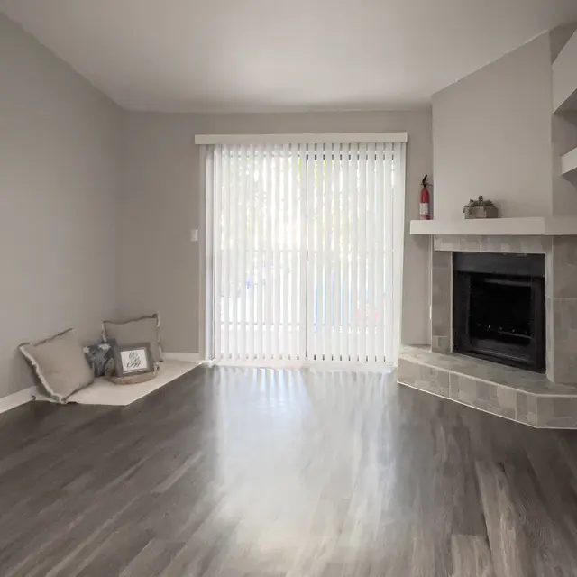 Cozy living room with gray walls, wooden floor, a fireplace, and large sliding doors with vertical blinds.