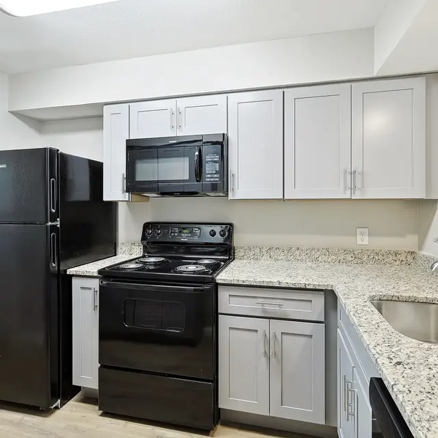 A modern kitchen featuring grey cabinets, black appliances, and a granite countertop.