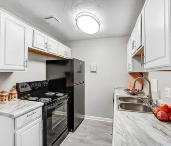 A modern kitchen featuring white cabinets, a black refrigerator, and an electric stove. There’s a gray countertop with a sink and some apples displayed in a bowl.