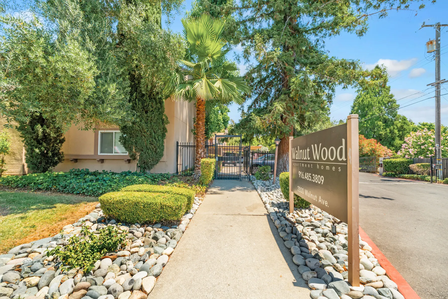 Entrance to Walnut Wood Apartments with greenery and rocks along the pathway.