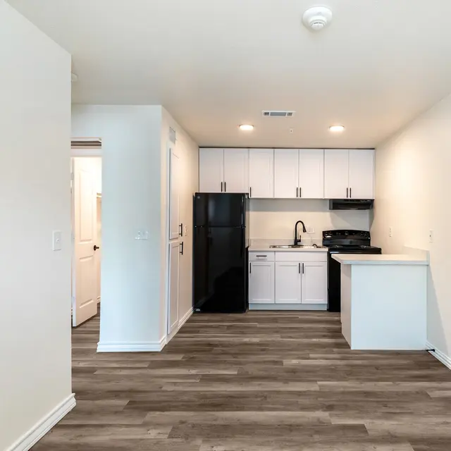 A modern kitchen featuring white cabinets and black appliances, with a light-colored wood floor and a small bar area.