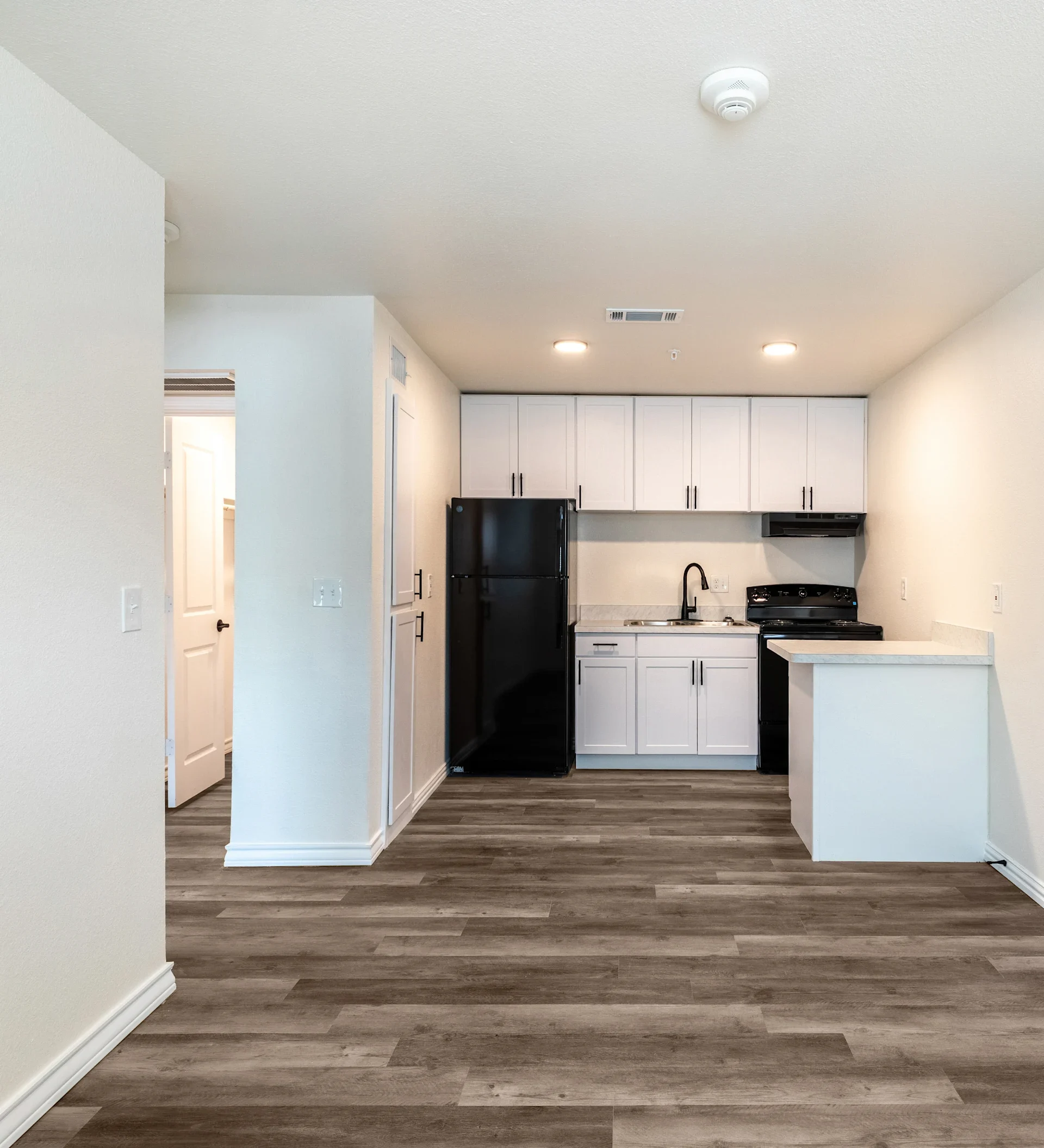 A modern kitchen featuring white cabinets and black appliances, with a light-colored wood floor and a small bar area.