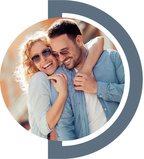 Happy Couple Embracing Outdoors A happy couple embracing outdoors, both wearing sunglasses. The woman has curly hair and is wearing a light blue top, while the man is shirtless under a light blue button-up shirt. They appear joyful and connected, with a blurred background of a sunny day.