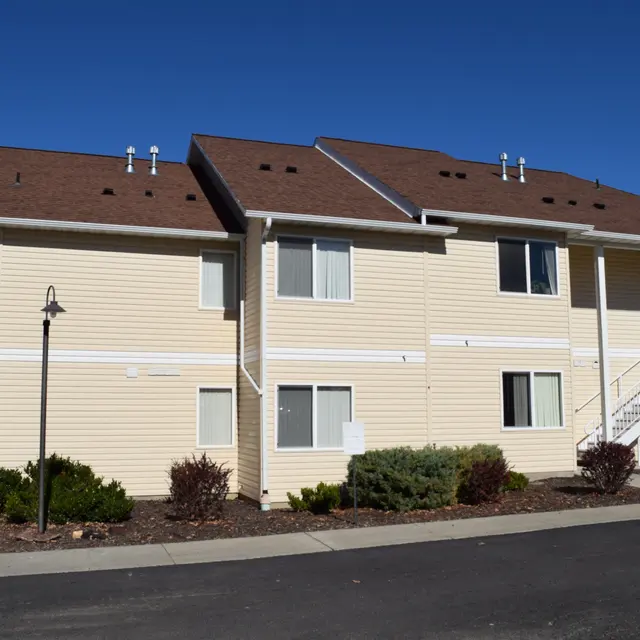 Two-Story Apartment Building Exterior Exterior view of a two-story apartment building with beige siding and brown roofs, featuring stairs and landscaping.