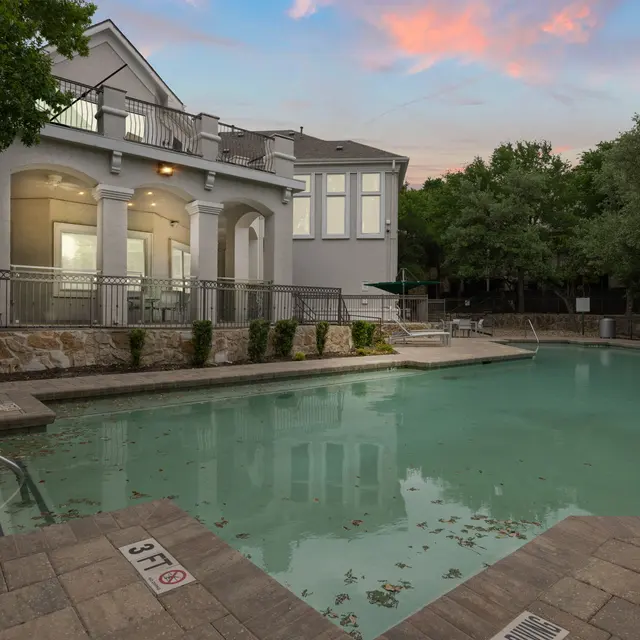A serene swimming pool area in the evening, surrounded by a residential building and green foliage.
