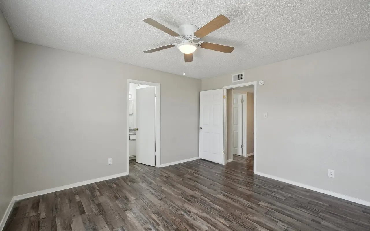 An empty bedroom featuring a ceiling fan and hardwood flooring. There are two doors leading to adjacent rooms.