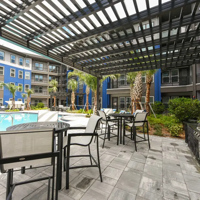 Outdoor pool area of a modern apartment complex with seating and palm trees.