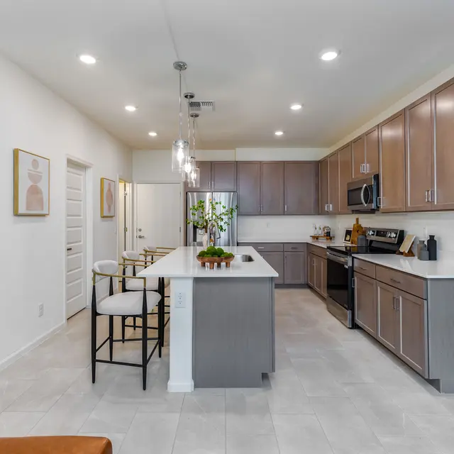 A modern kitchen featuring a large island with a seating area, stainless steel appliances, light wood cabinetry, and a neutral color palette.