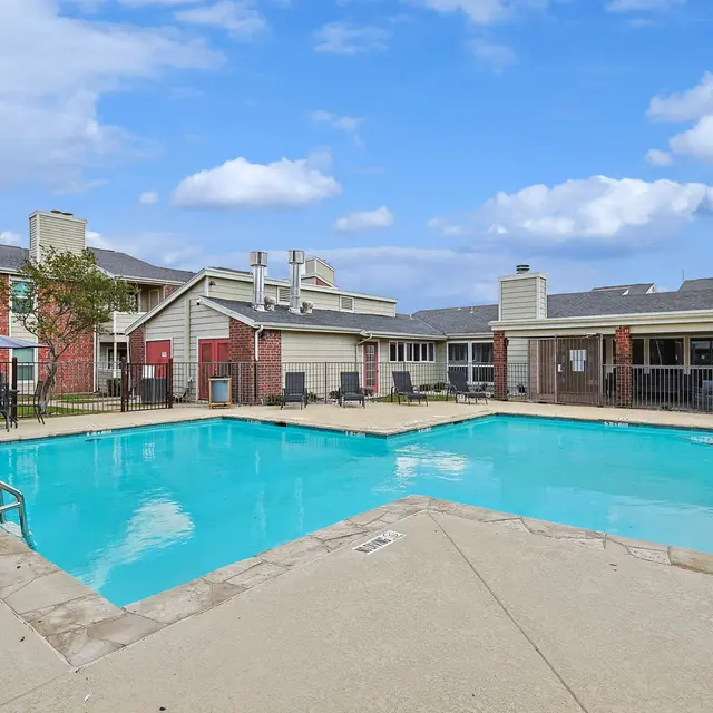 Outdoor swimming pool surrounded by lounge chairs and a brick apartment complex.