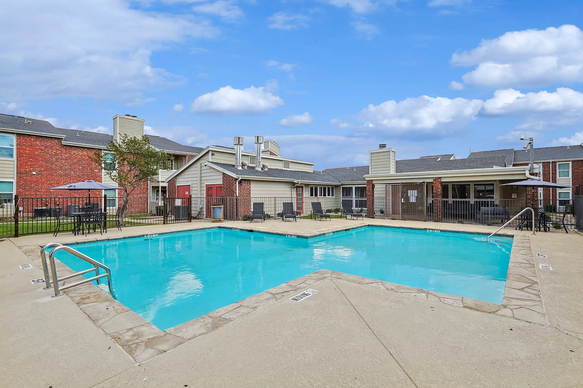 Apartment Complex Swimming Pool Outdoor swimming pool surrounded by lounge chairs and a brick apartment complex.