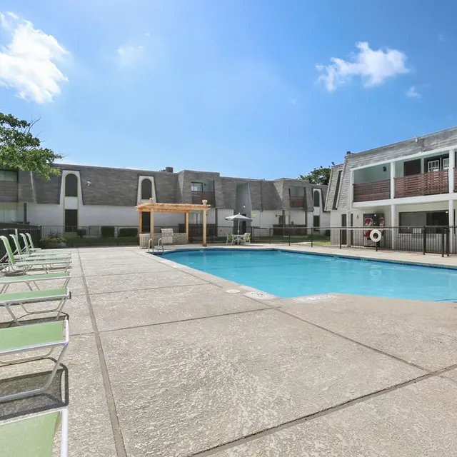 Swimming pool area at an apartment complex with lounge chairs and a pergola.