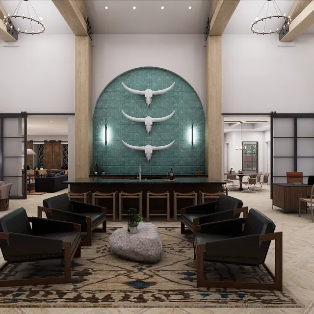 A spacious and modern lobby with wooden beams and large windows, featuring a large decorative wall with three mounted horns. The seating area includes four dark chairs arranged around a light rug with a central coffee table and a decorative stone. The lobby is well-lit and has a welcoming atmosphere, with a mix of seating options including a small table and chairs on the side.