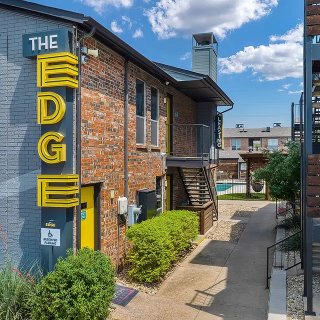 Exterior view of a building named 'The Edge' with yellow signage, surrounded by greenery and a pool area visible in the background.