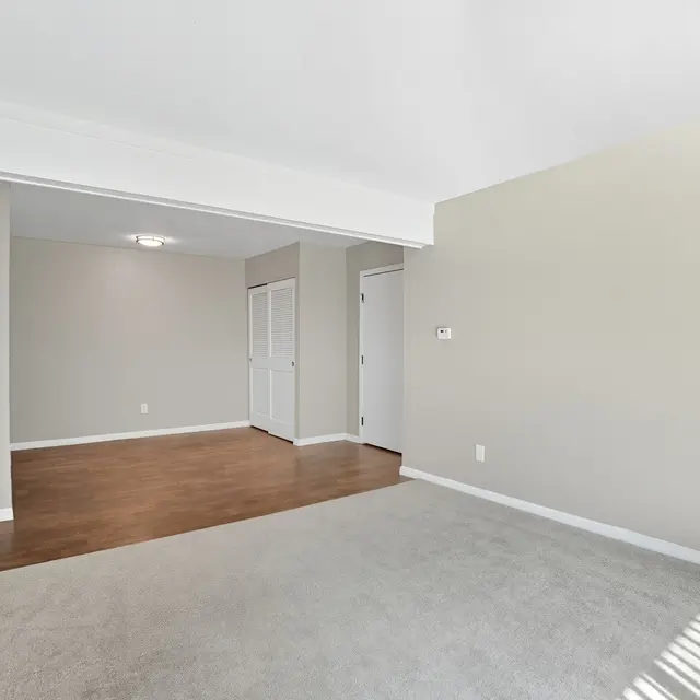 Empty living room with carpet and wooden floor, featuring a wall and a doorway
