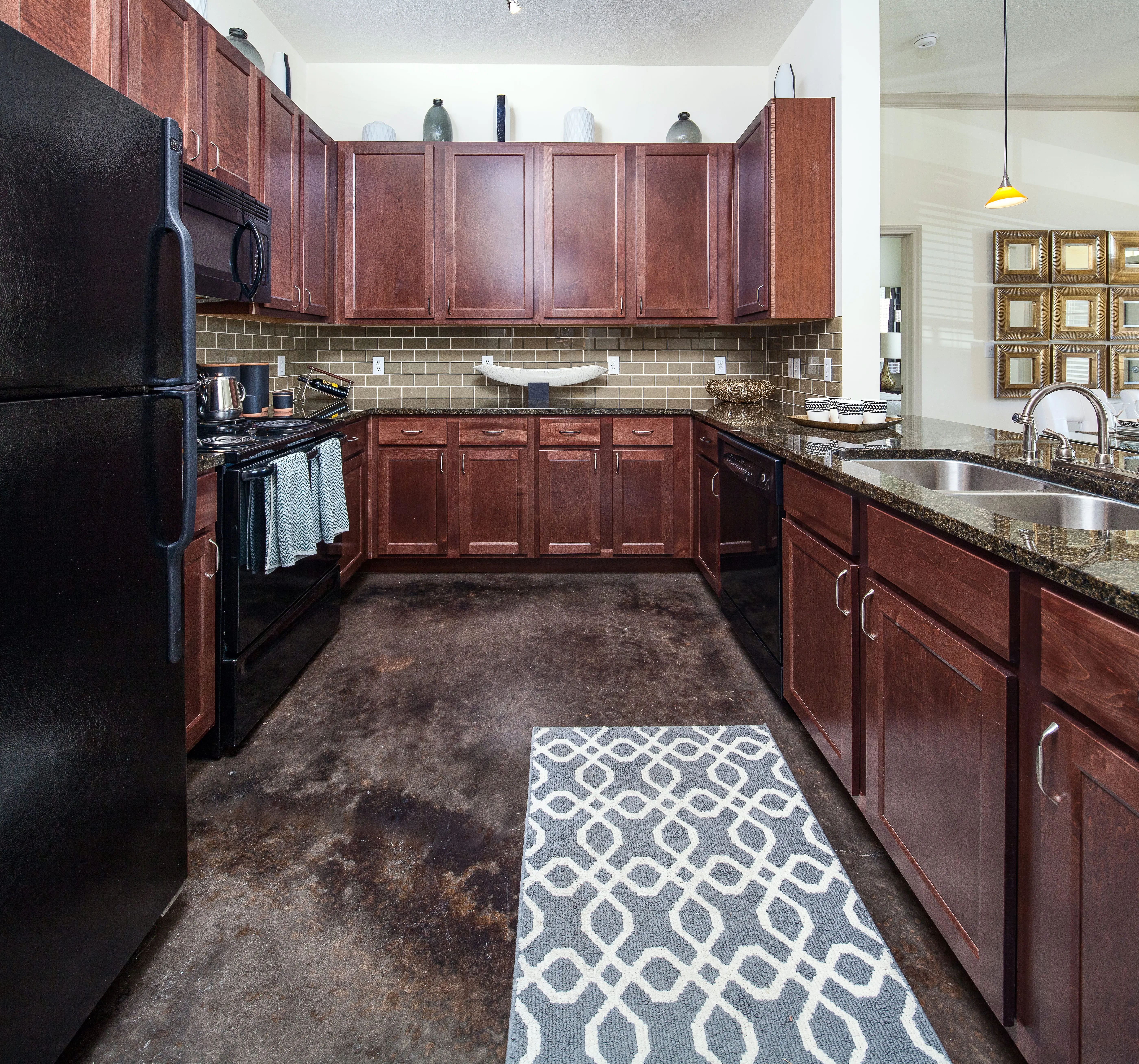 A spacious kitchen featuring dark wood cabinetry, a black refrigerator, and a dual sink with a contemporary design. The countertop is made of granite and there is a geometric patterned rug on the floor.