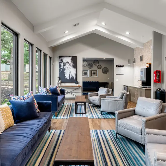 A modern living area with large windows, featuring blue and gray seating, a wooden coffee table, and artistic wall decor.