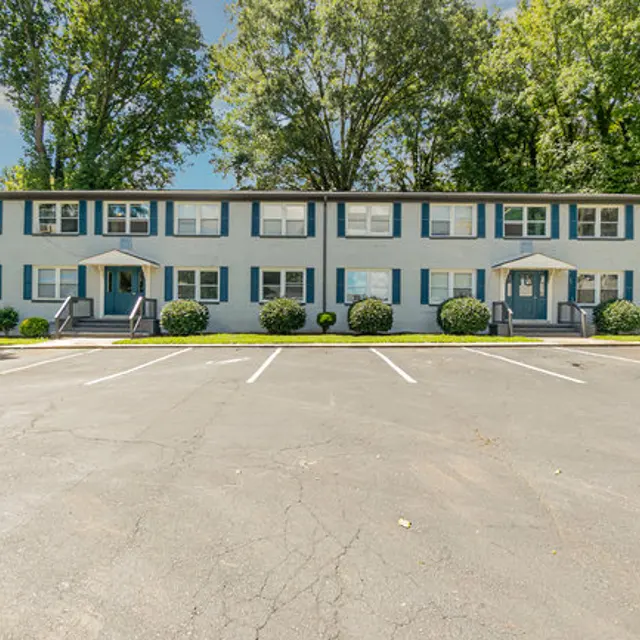 Exterior view of a two-story apartment building with blue siding, white trim, and several parking spaces in front.