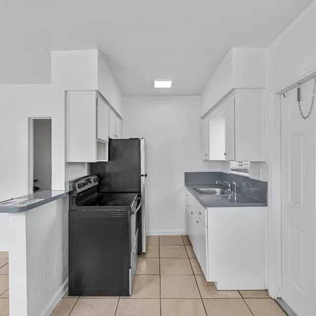 A modern kitchen featuring white cabinets, gray countertops, and tiled flooring. The kitchen has an open layout with a view towards an adjoining room.
