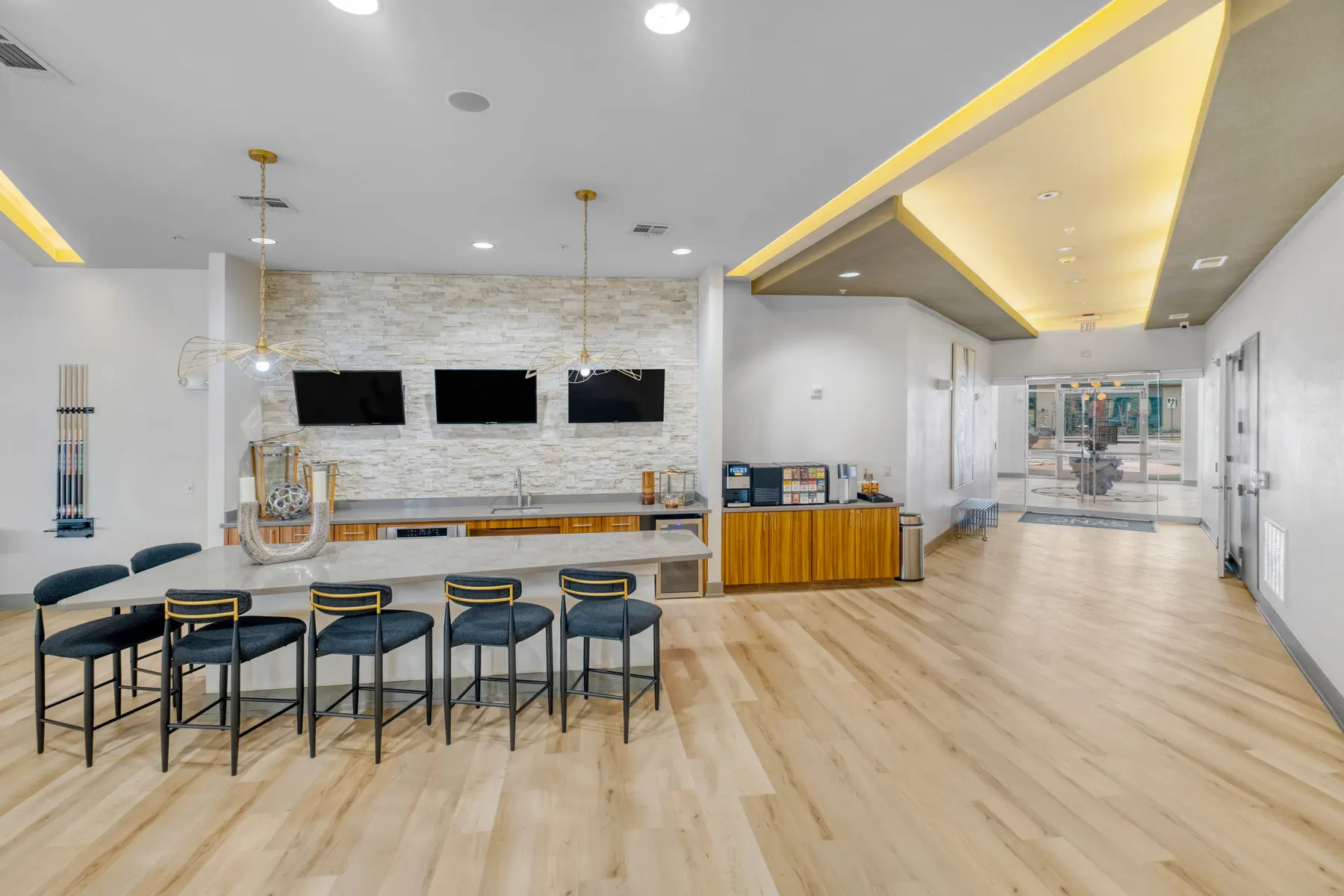 A modern community amenity space featuring a large bar counter with seating, wall-mounted televisions, and a stylish design.